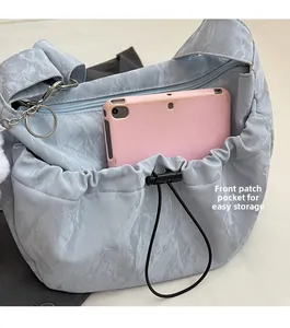 Detail view of light blue nylon shoulder bag with front drawstring pocket holding a tablet