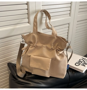 Detail of beige pleated drawstring tote bag with small front pocket on leather surface
