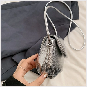 Detailed view of silver metallic textured crossbody bag with rounded flap and thin strap