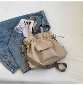 Close-up of beige drawstring tote bag featuring front flap pocket and adjustable strap