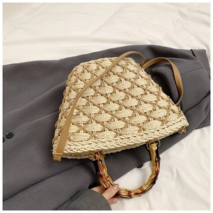 Detail of straw woven bag featuring bamboo-style handle and brown leather strap on blazer