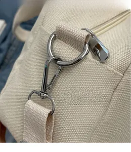 Close-up of durable silver metal hook and woven strap on a beige canvas tote bag