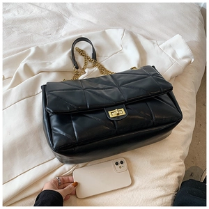 Detail of black quilted leather shoulder bag with gold chain strap on white fabric
