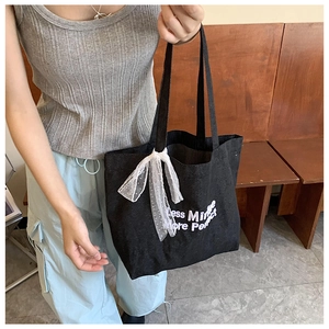 Detailed macro view of black canvas tote with white lace bow and elegant quote printing
