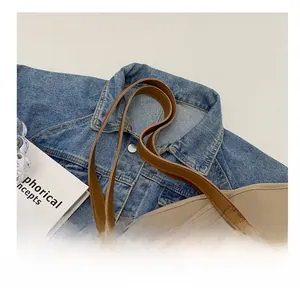 Detail of a beige canvas tote bag showing brown leather straps on a denim jacket