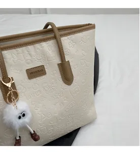 Detail of cream tote bag featuring 3D embossed patterns and a white furry monster pendant