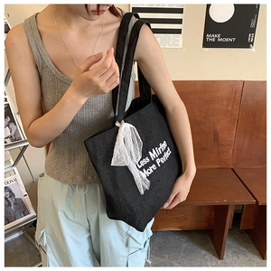Detail of black denim tote bag with white bow and minimalist slogan embroidery