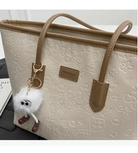 Detail of cartoon embossed pattern and plush charm on off-white large tote bag