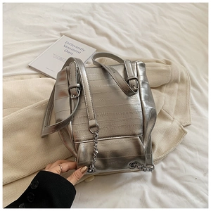 Detailed view of silver backpack with crocodile texture and metallic chain decoration