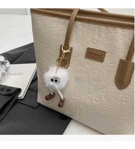 Close-up of off-white tote bag with cartoon heart embossing and fuzzy monster charm