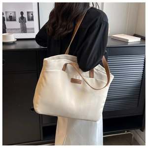 Detail of a beige canvas tote bag featuring brown leather handles and brand logo tag