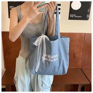Detail of blue denim tote bag with white embroidery and lace bow decoration