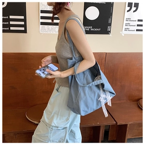 Detail of light blue denim bucket bag with white lace ribbon and Less More embroidery