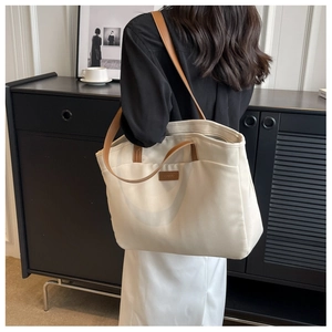 Detail of white canvas tote bag with brown leather shoulder straps and brand logo patch