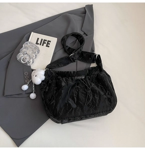 Detail of black pleated tote bag with drawstring closure and white cloud plush charm