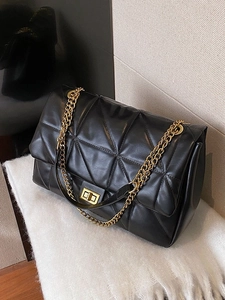 Quilted black shoulder bag with gold chain strap and square metal lock on plush background