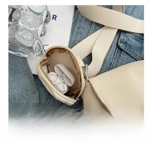 Detail of round coin purse on beige shoulder bag strap showing earbud storage