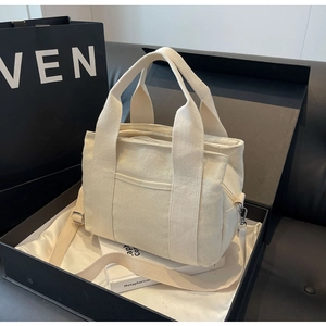 Detail of off-white canvas tote bag with adjustable shoulder strap and top zipper closure