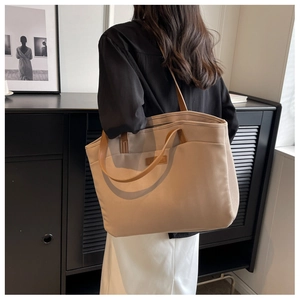 Side view of a large beige canvas tote bag with brown leather handles on shoulder