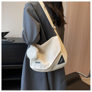 Détail du sac messager en toile beige avec bandoulière large et porte-monnaie rond attaché