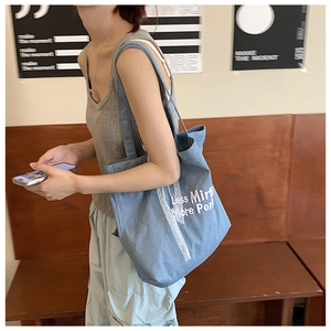 Close-up of blue denim tote bag with white embroidery and mesh ribbon on model