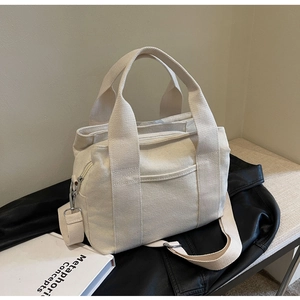 Detail of adjustable strap, sturdy handles, and metal zipper on beige canvas tote bag