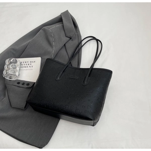 Flat lay of black embossed tote bag with cartoon patterns on white fabric background