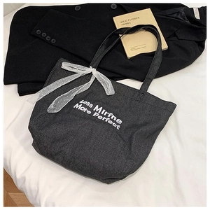Detail of black canvas tote bag with white lace bow and elegant slogan embroidery
