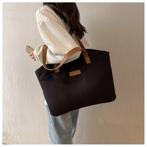 Detail of contrast stitch brown leather strap and embossed logo on black canvas tote bag