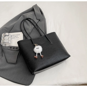 Detail of black embossed tote bag with cartoon patterns and a white fuzzy monster charm