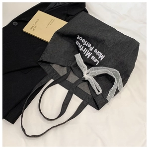 Detail of grey denim tote bag with embroidery, white mesh bow, and text on white fabric
