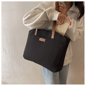 Macro view of a large black canvas tote bag showing interior space and brown leather handles