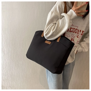 Detail of black canvas tote bag showing brown leather handles and brand logo tag