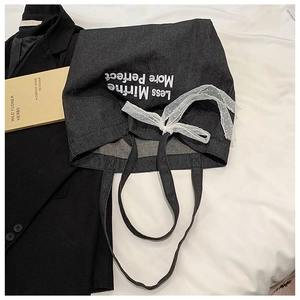 Detail of dark grey canvas tote bag with lace bow and lettering on bed linen