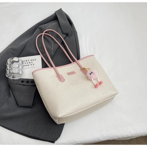 Macro detail of creamy white leather tote featuring embossed patterns and pink charm