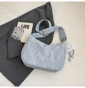 Detail of light blue pleated shoulder bag with cloud charm on grey blazer backdrop