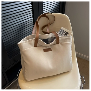 Detail of canvas tote bag showing brown leather handles and brand tag on a shell chair
