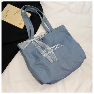 Detail view of light blue denim tote bag with white embroidery and lace bow decoration