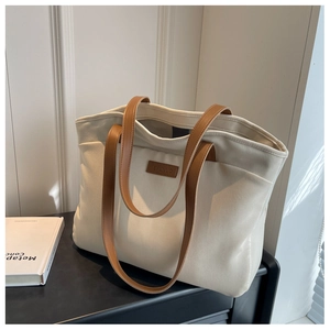 Close-up of cream canvas tote bag featuring brown leather straps and branded leather patch