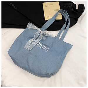 Flat lay of denim tote bag with white lace bow and Mirne Perfect embroidery detail
