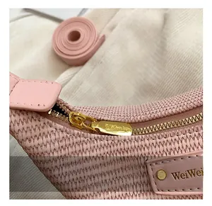 Gros plan du sac en paille rose montrant le zip doré et l'étiquette de marque en cuir