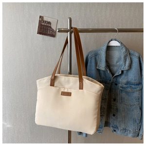 Detail of canvas tote bag with brown leather straps and stitched brand label on front