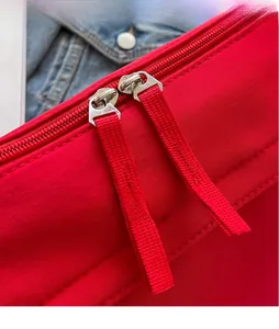 Macro detail of the red bag featuring dual silver metal zippers with woven strap pullers