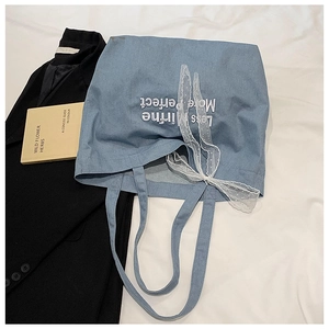 Detail of light blue denim tote bag with white lace bow and embroidered text