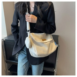 Close-up of beige canvas shoulder bag featuring a brown leather logo and small round pouch