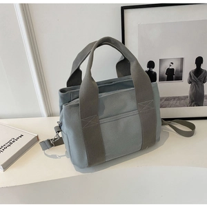 Detail view of the light grey-blue canvas tote with reinforced handles and metal D-ring