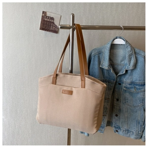 Detail of beige canvas tote bag with brown leather straps and brand logo for commuting
