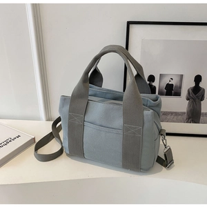 Detail of light blue canvas tote bag featuring reinforced handles and adjustable strap