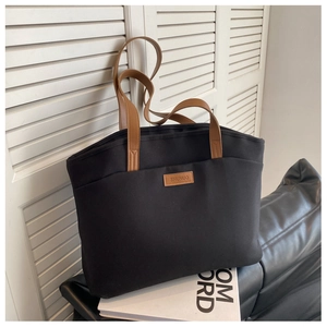 Detail of canvas tote bag showing brown leather handles and brand nameplate on black fabric