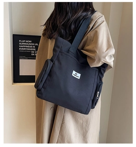 Close-up of black canvas tote bag featuring white fashion label and side zipper pocket